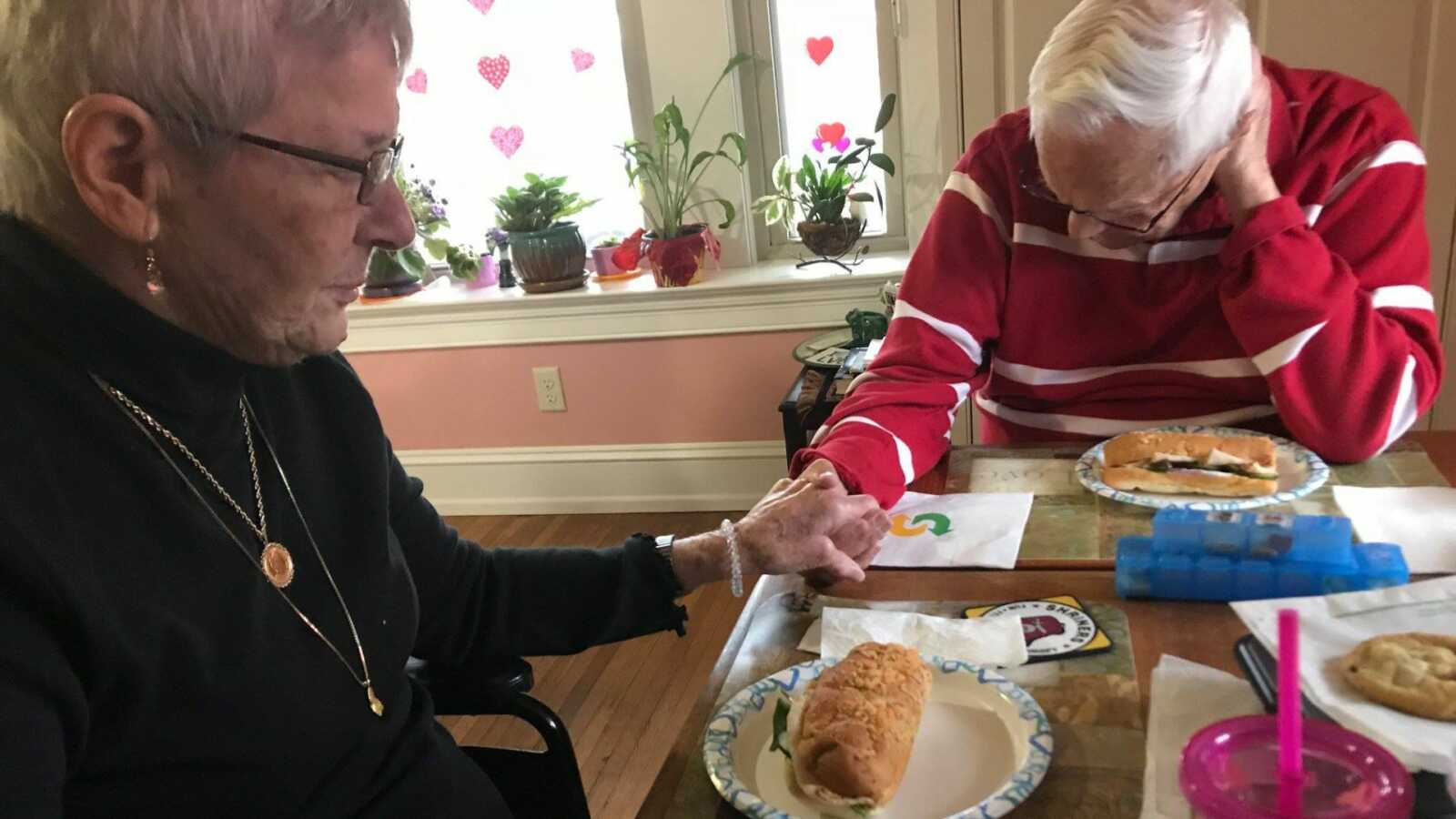 elderly couple sitting at table and praying over food