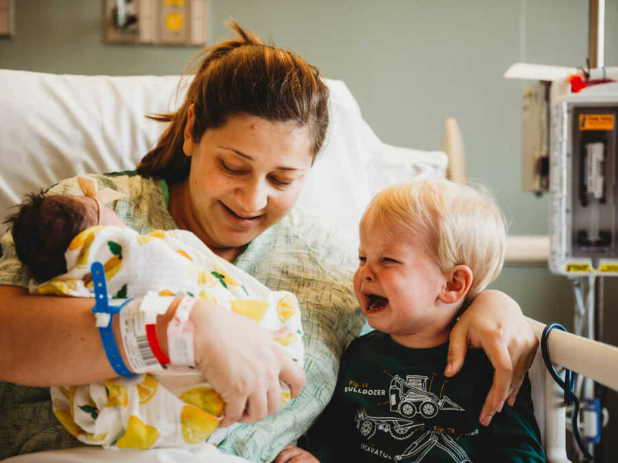 mom with crying son and newborn daughter in hospital bed