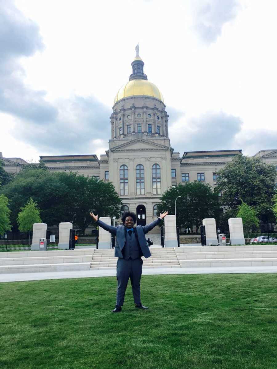 Teen in prom suit raising arms in front of Atlanta building