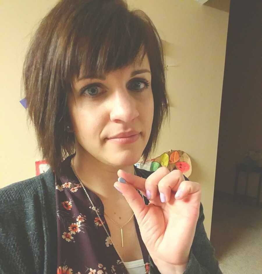 Woman holding up little blue pill that is an antidepressant in selfie