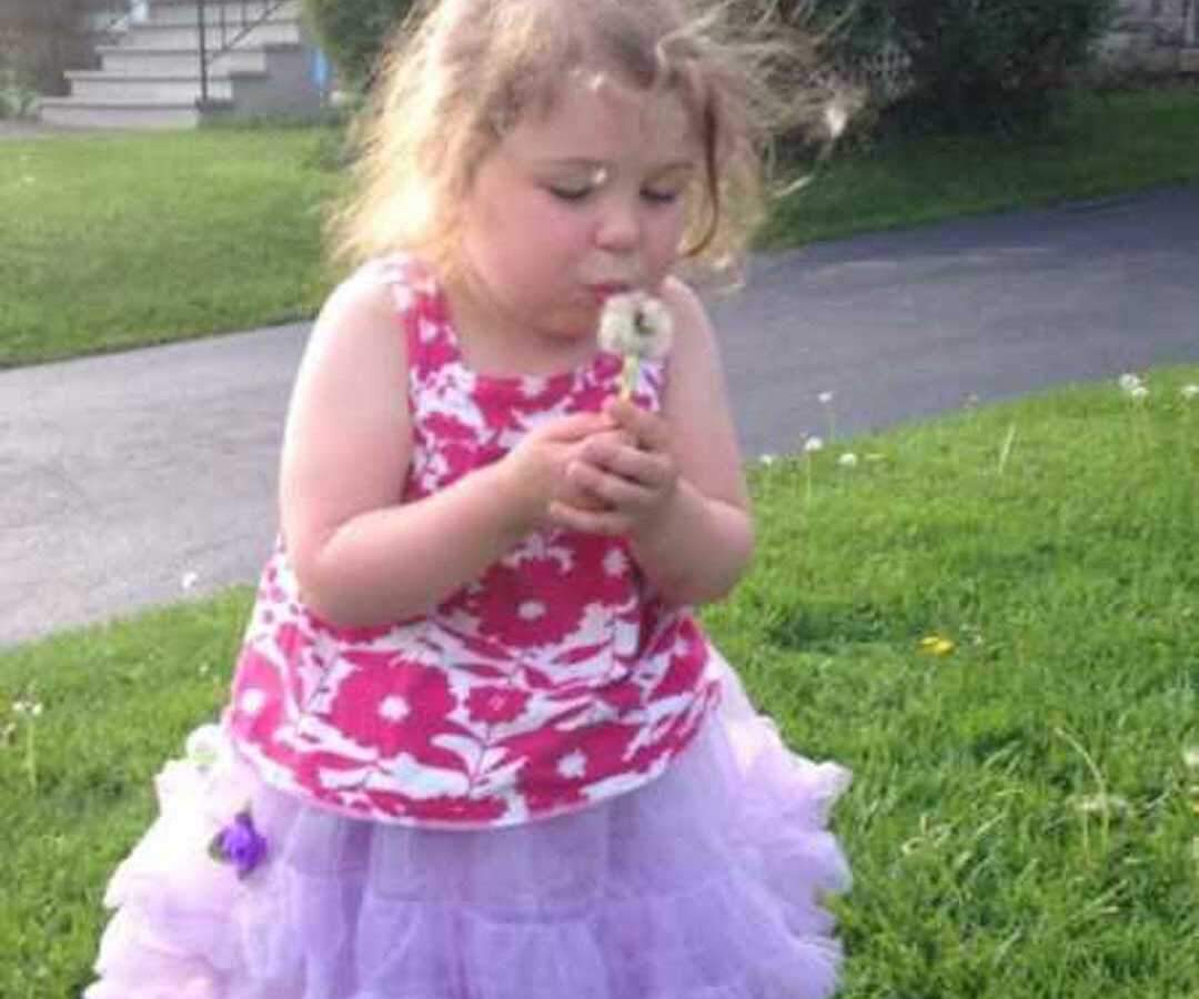 young girl in costume dress blowing dandelion