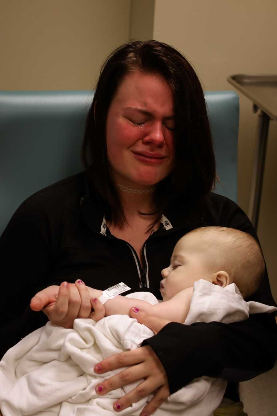 Mother kneels on ground resting her head on 8 month old son