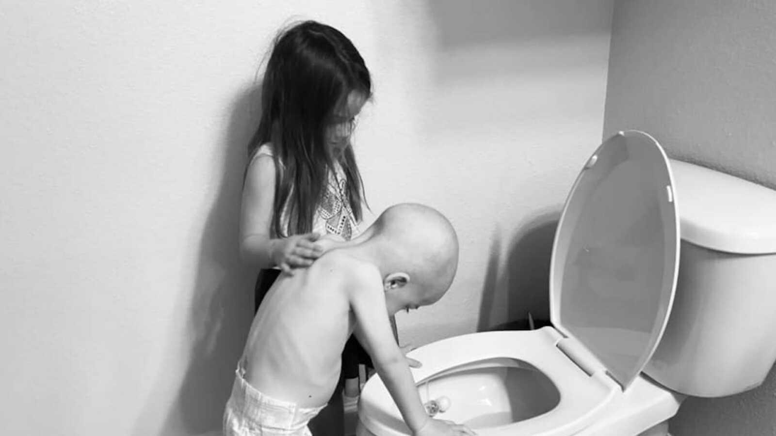 young, sick boy standing at toilet with sister by his side