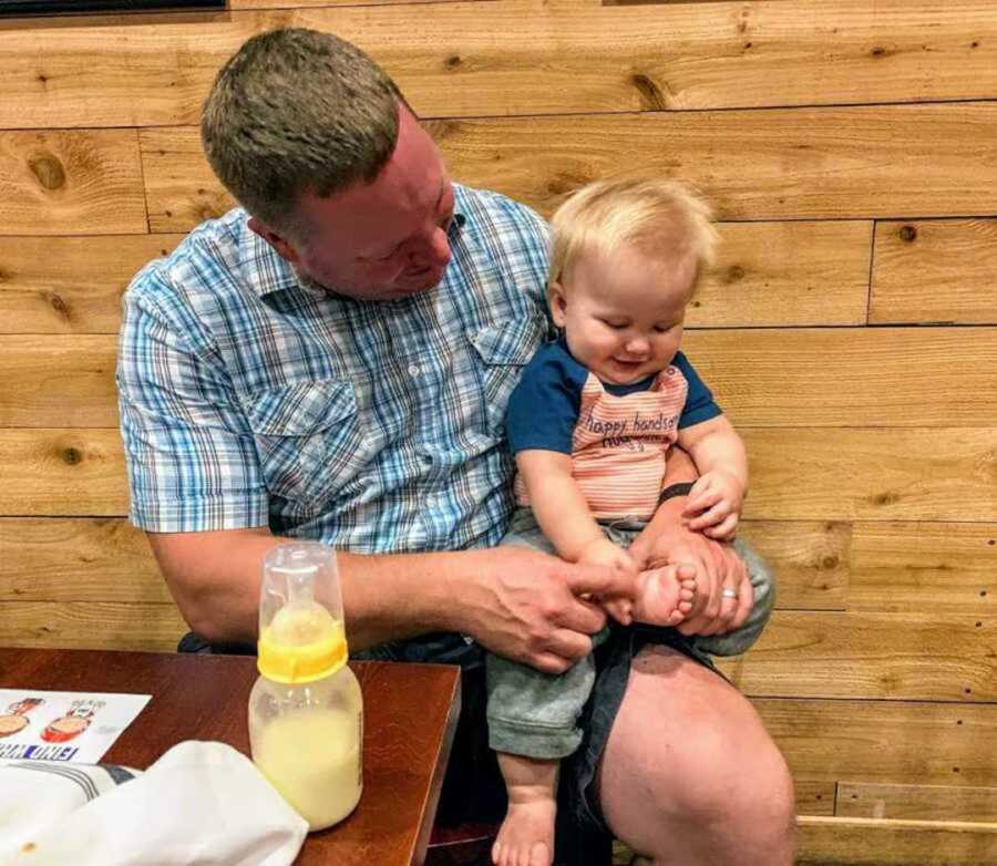 dad tickling infant boy's feet at restaurant