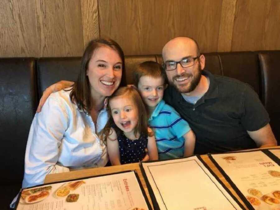 Family of four smiling at restaurant seating booth