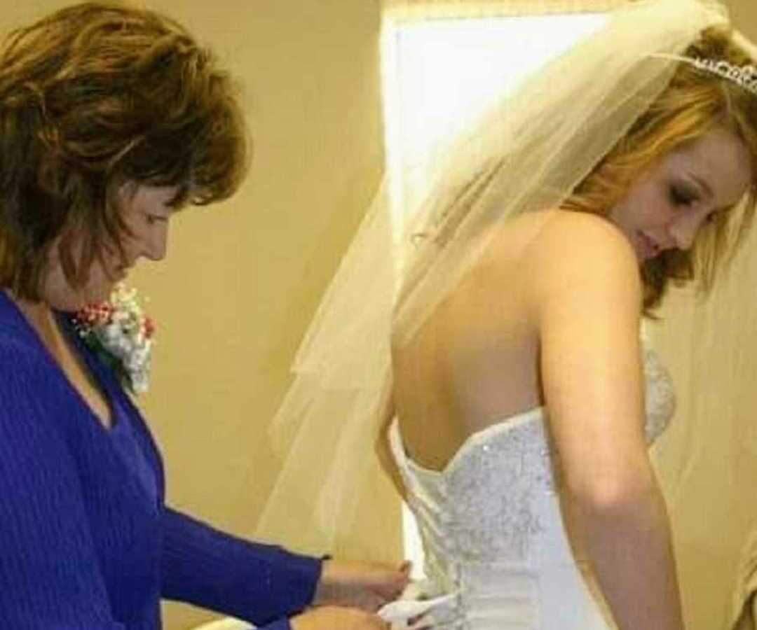 mom tying back of daughter's wedding dress