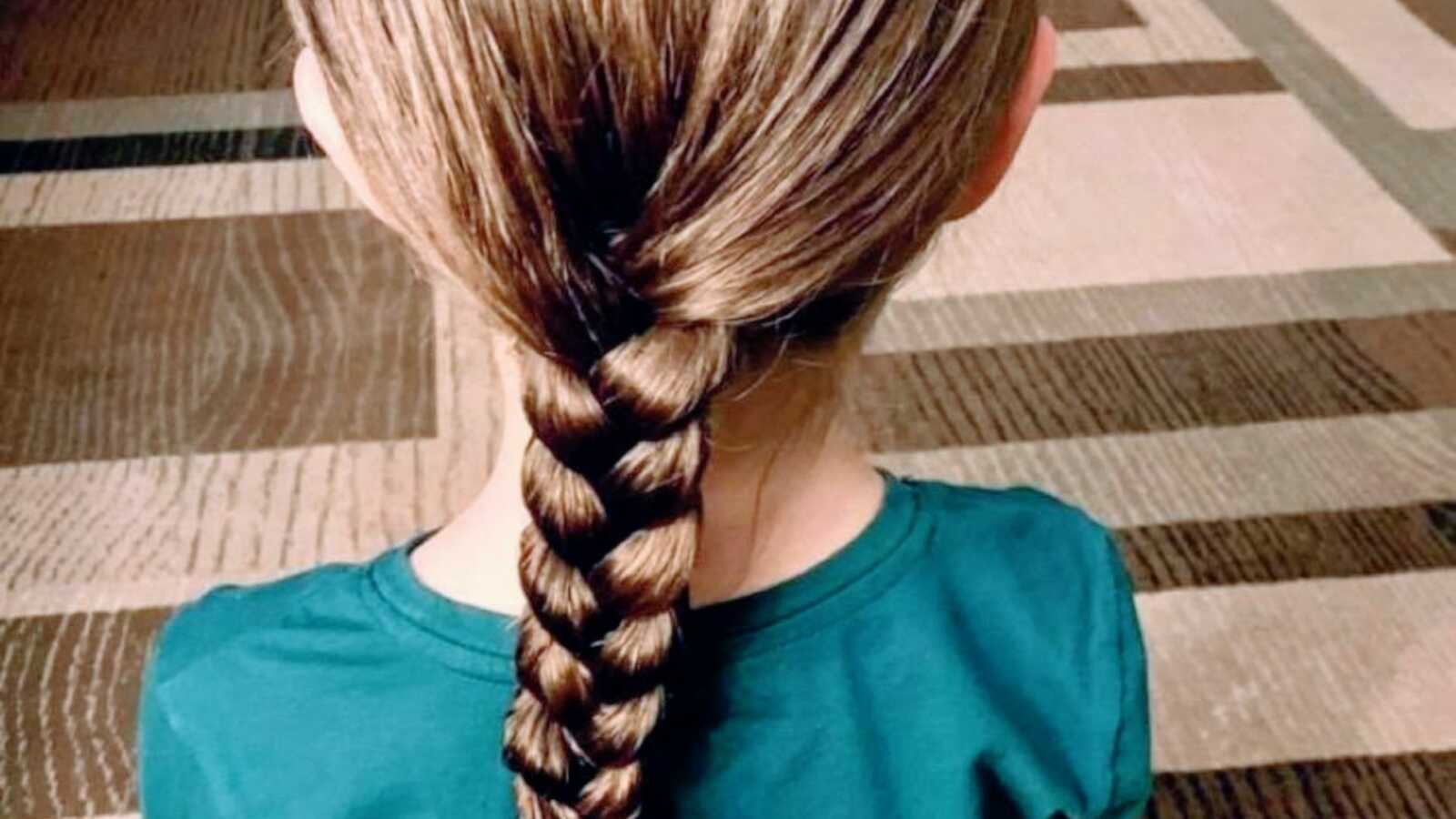 young girl sits on floor with hair in long braid