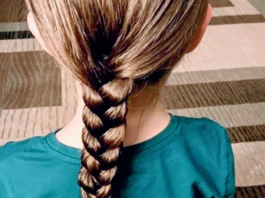 young girl sits on floor with hair in long braid