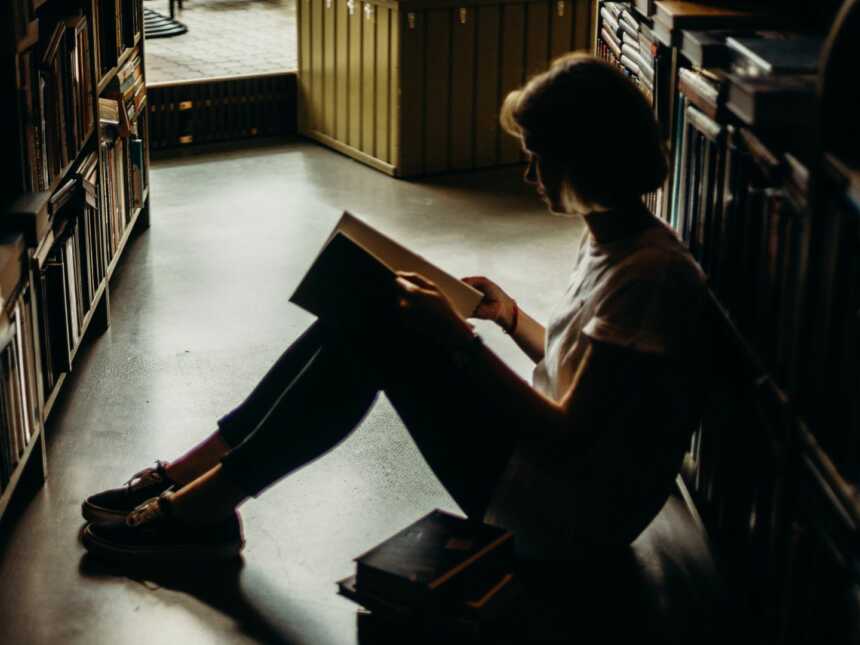 Girl with short hair reading book on library floor