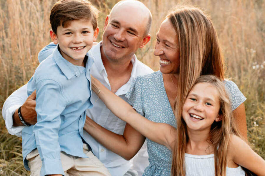 family smiling while sitting outside in field