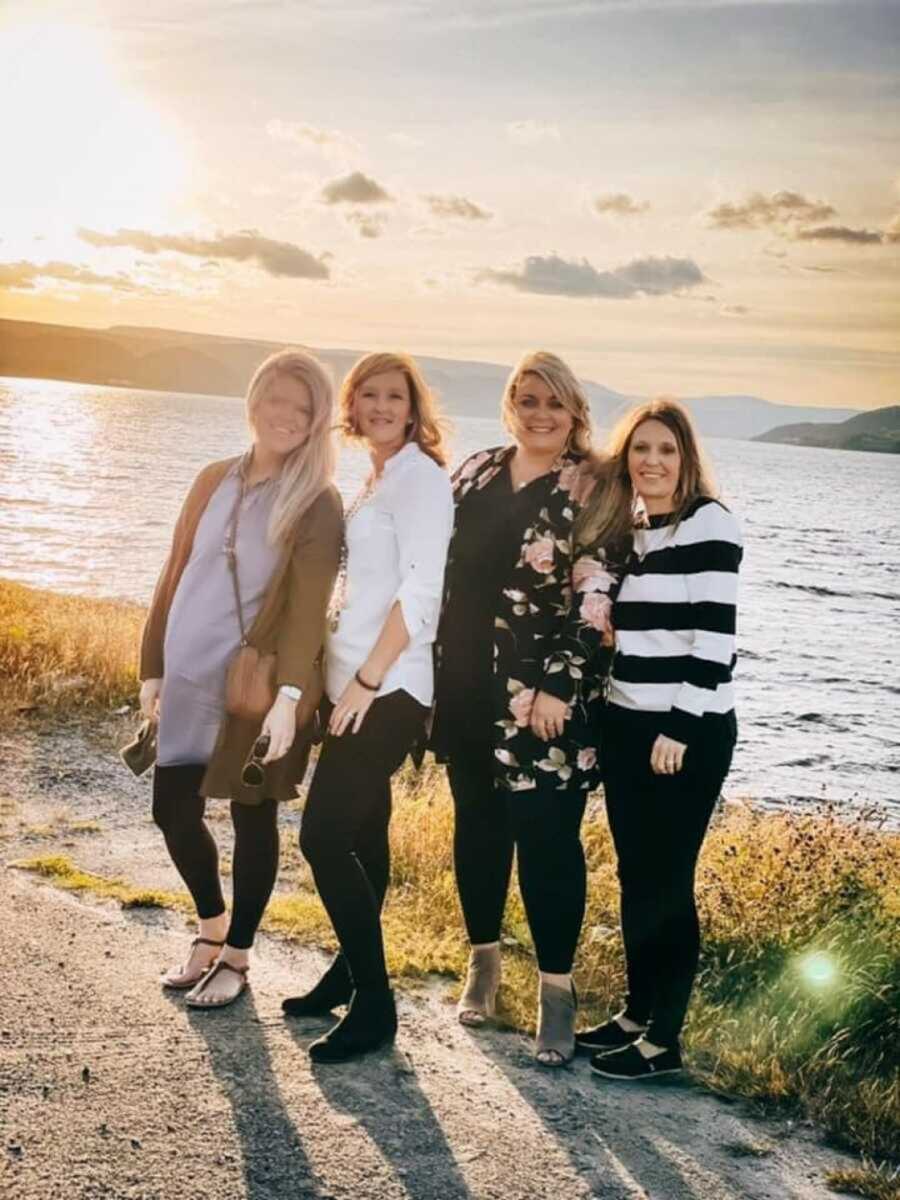 four women standing outside in front of water