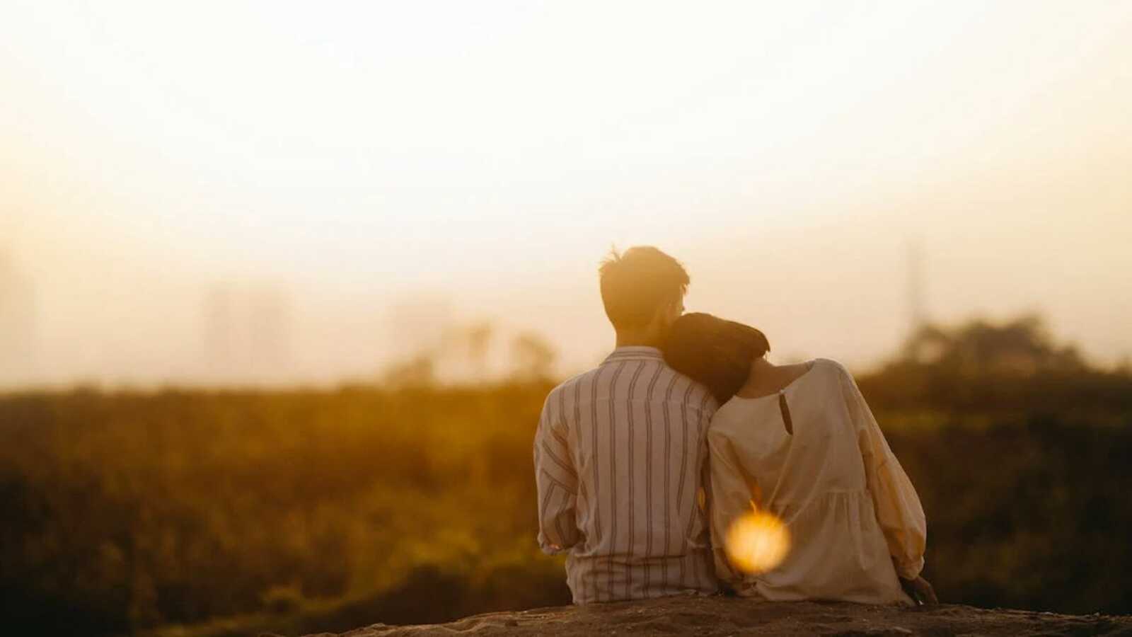Woman leaning head on man's shoulder in front of sunset