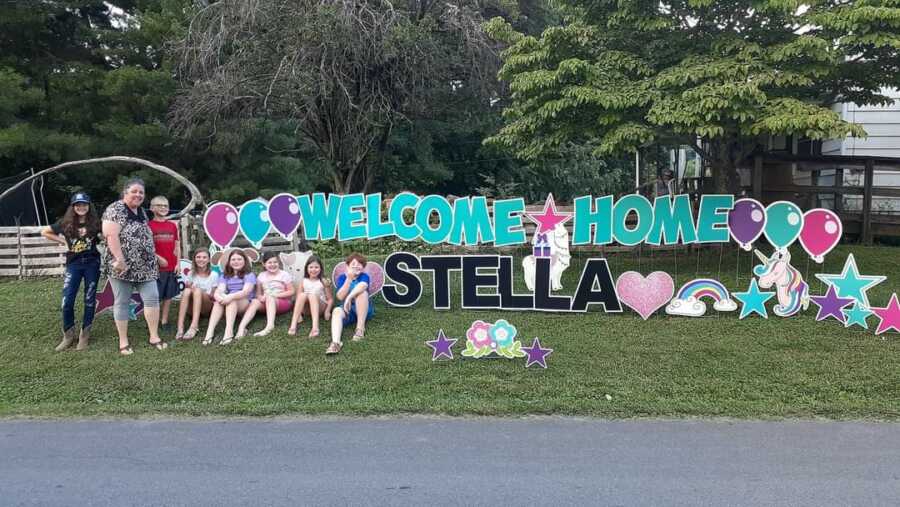 Family sitting alongside welcome home sign