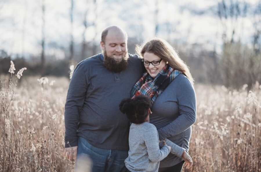 Adoptive parents smiling at foster daughter in field