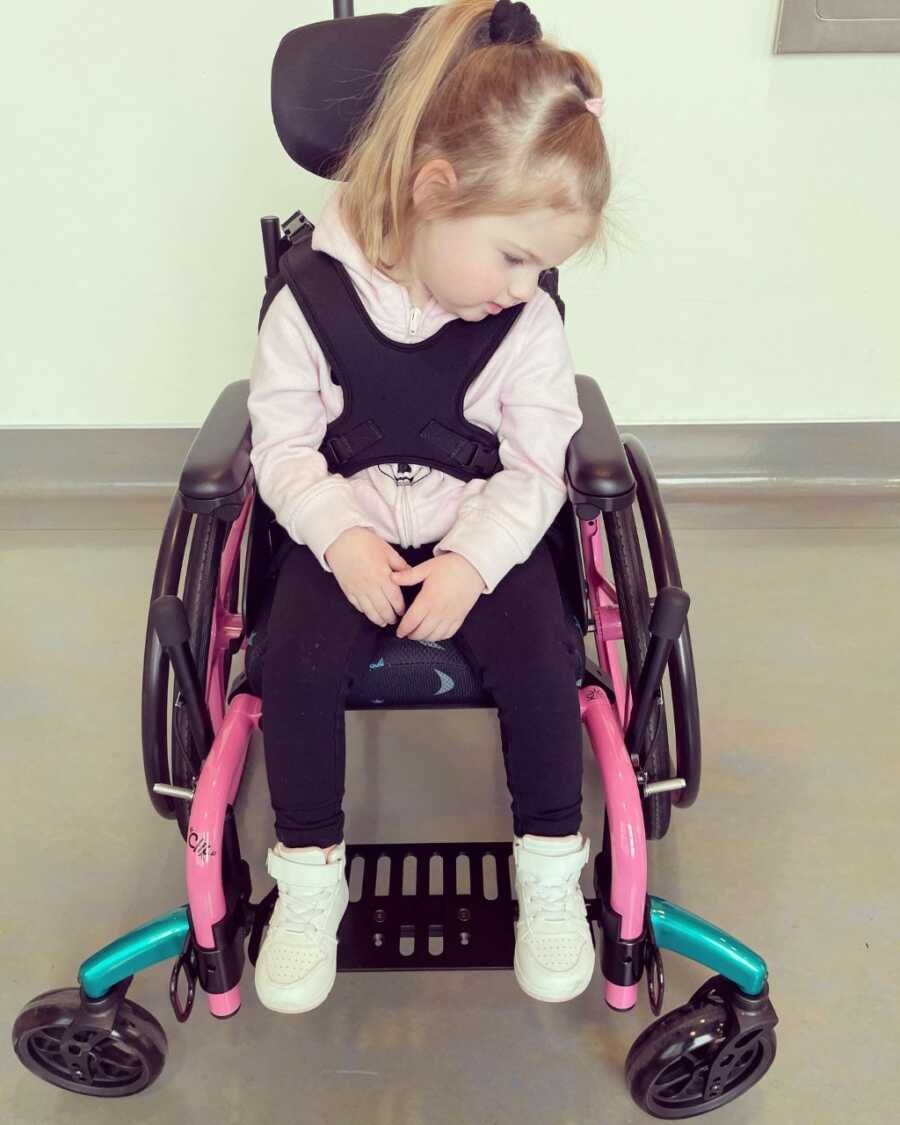 blonde girl sitting in blue and pink wheelchair