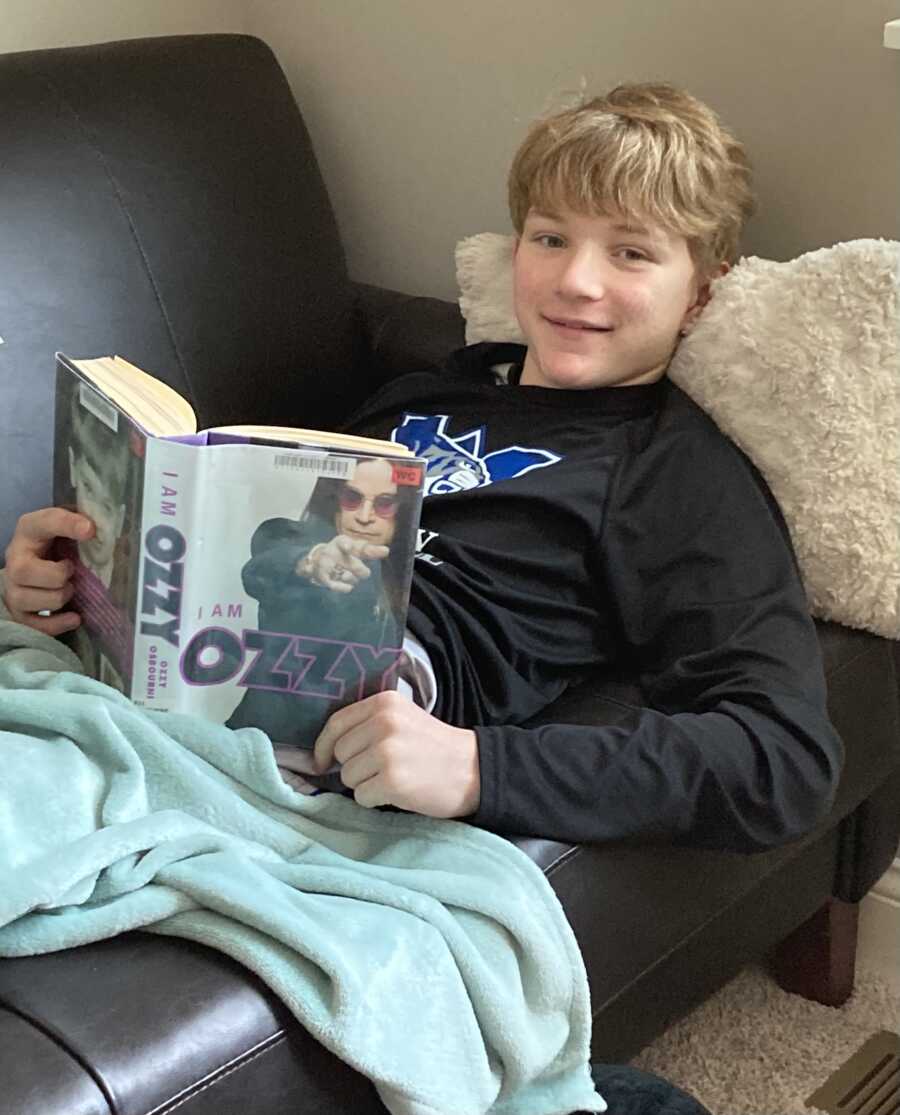 Boy sleeping on black leather couch while reading Ozzy Ozborne book
