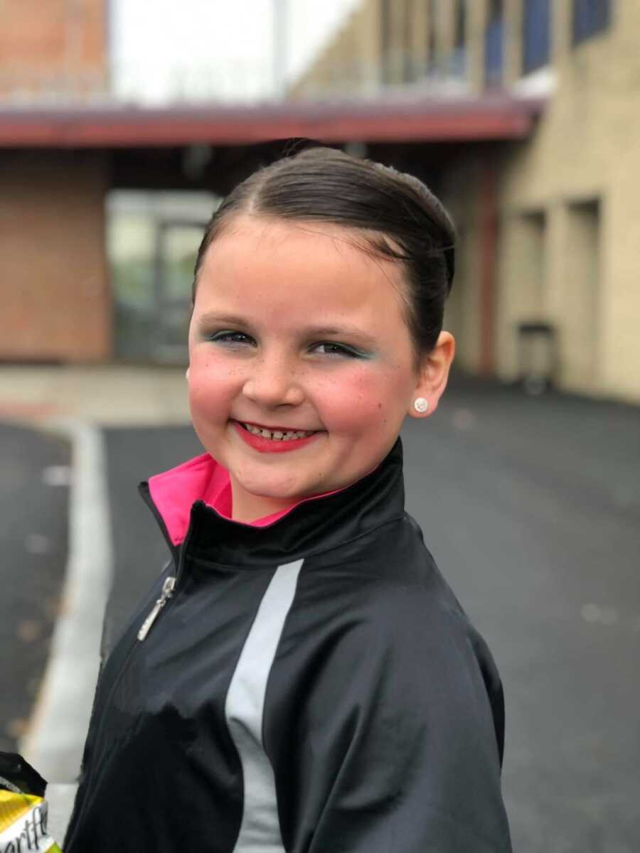 Little girl in dance jacket smiling in parking lot