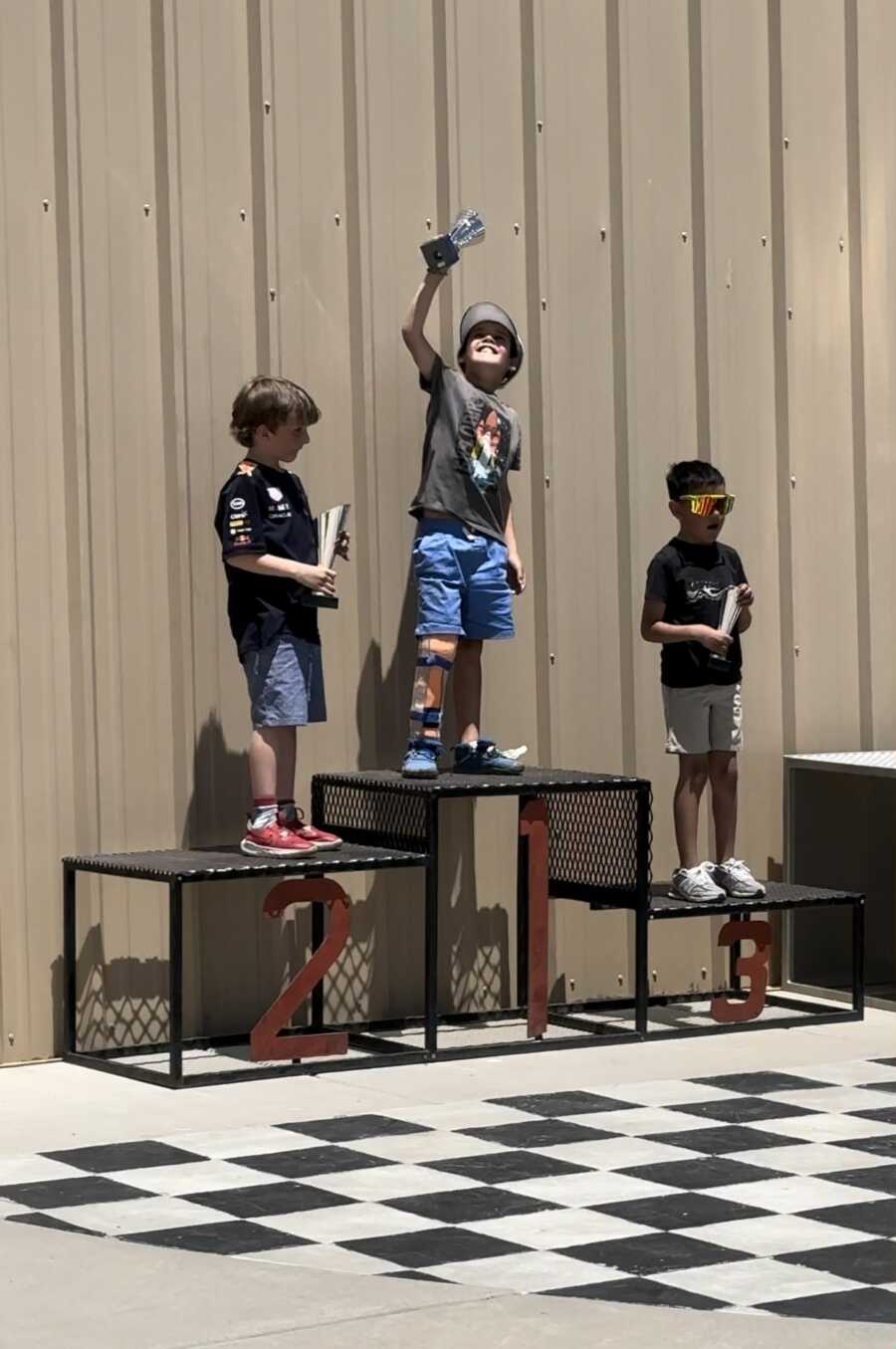 Boy standing on podium proudly holding racing tophy