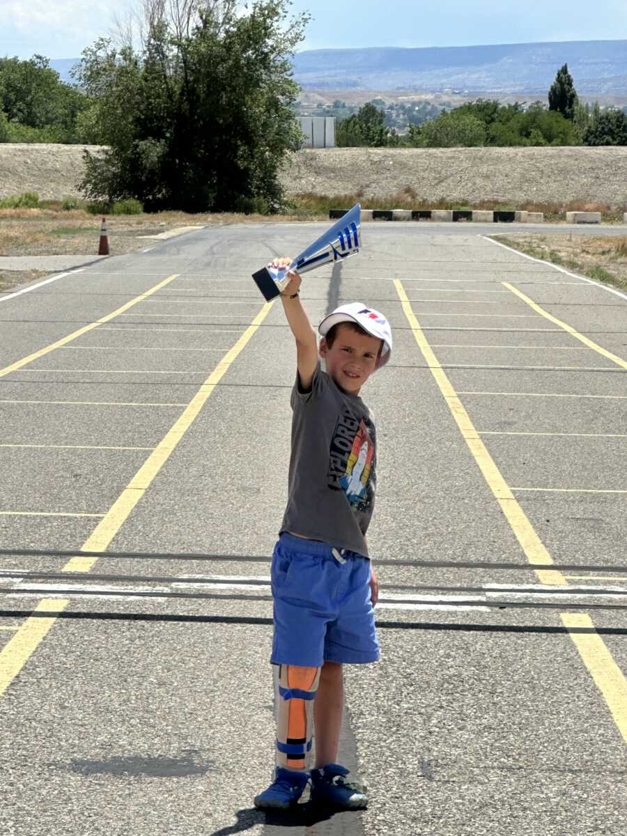 Boy holding racing trophy in parking lot