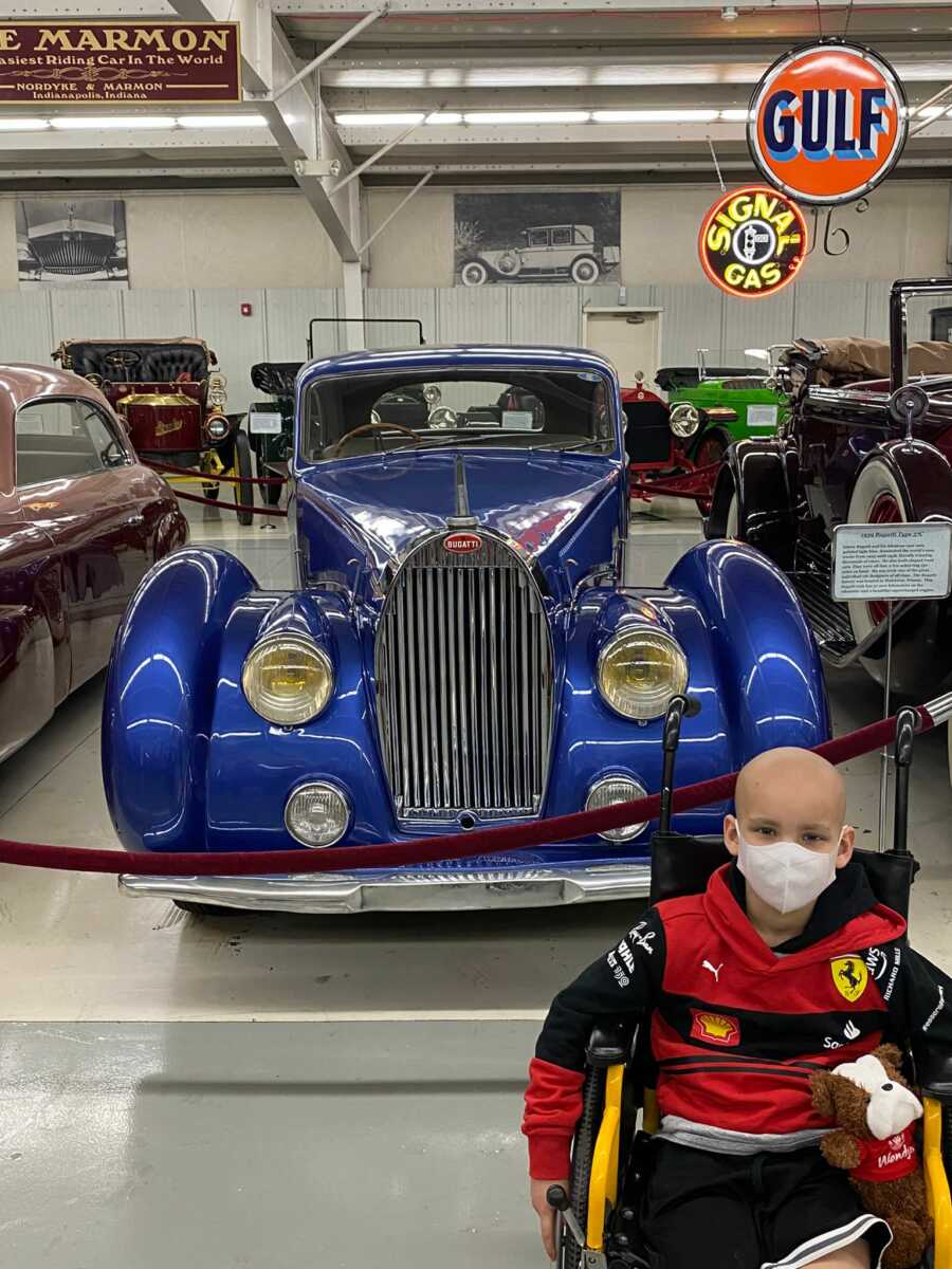 Young boy in wheelchair sitting next to blue vintage car