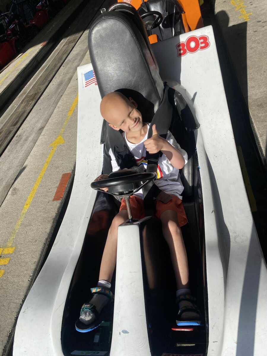 Young cancer patient giving thumbs up inside go-kart