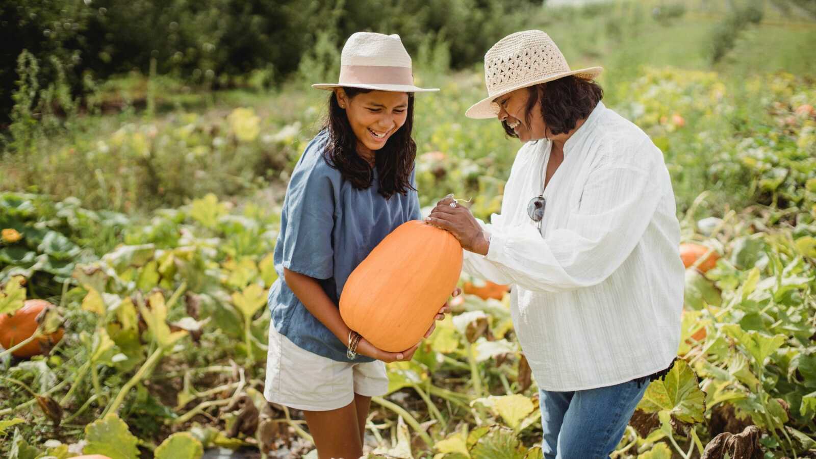 mom and pre-teen daughter pick out a pumpkin from a pumpkin patch