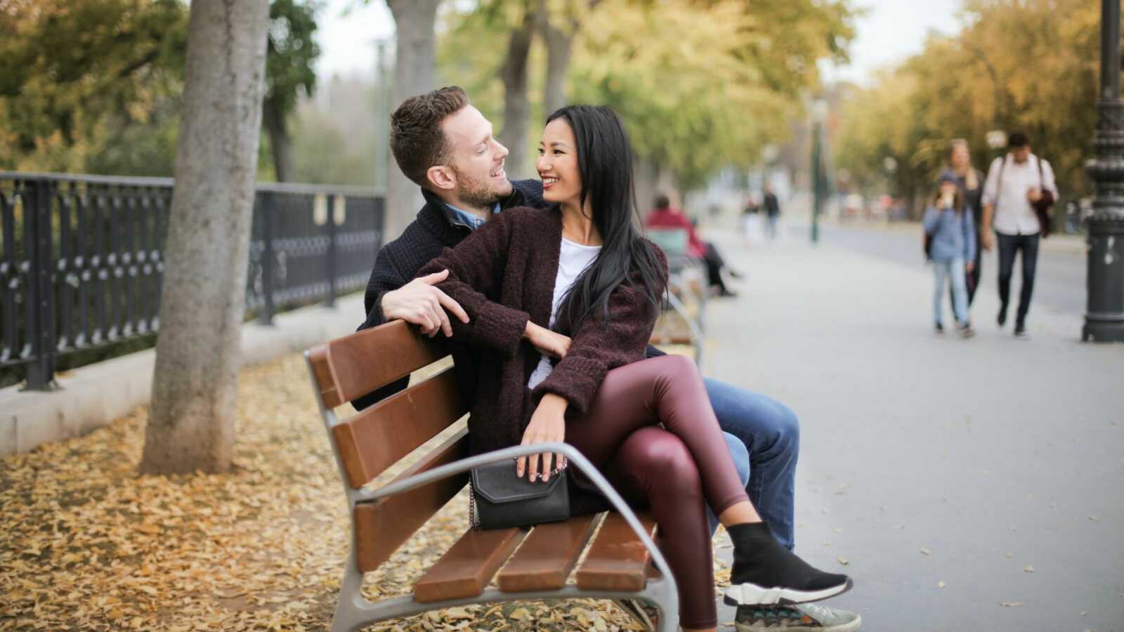 a couple sits next to each other on a wooden bench outside