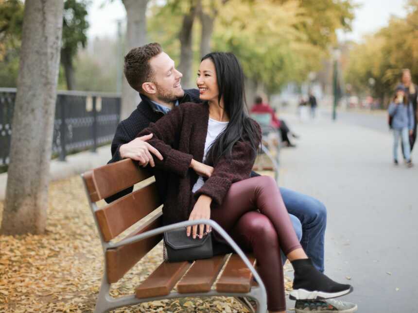 a couple sits next to each other on a wooden bench outside
