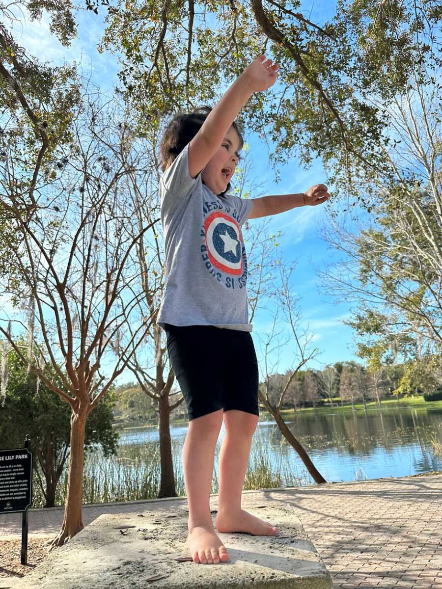 Child raises her arms abover her head outside