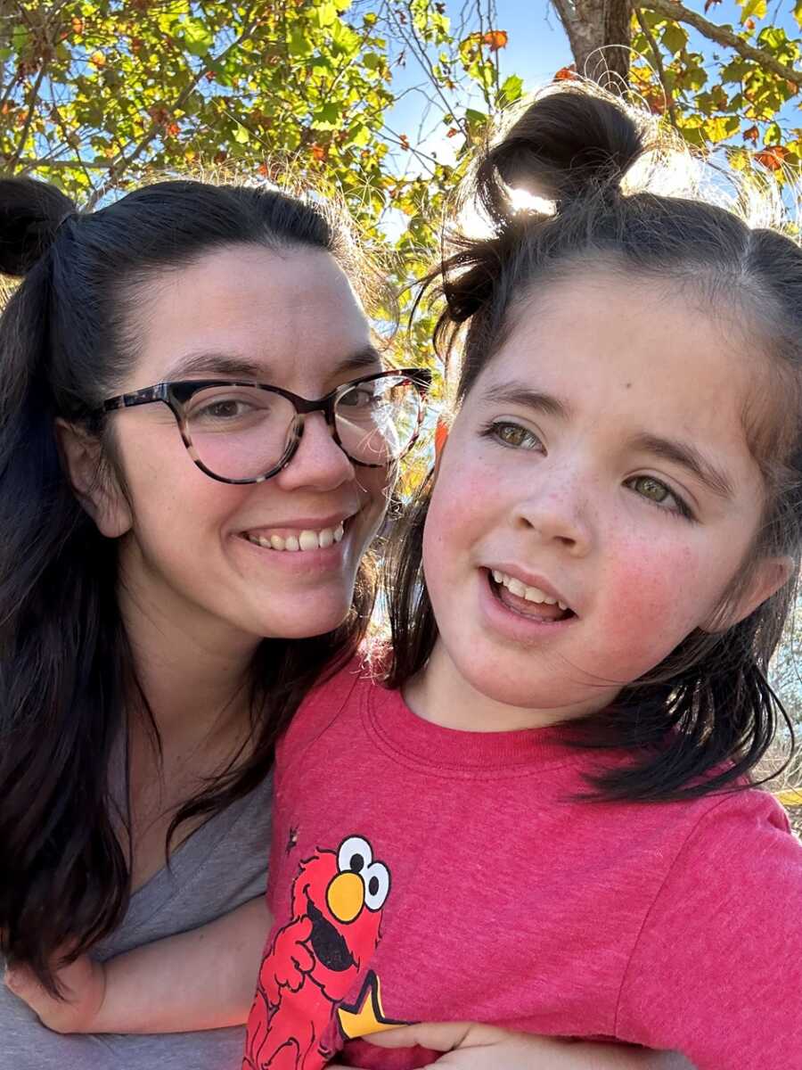 Mother and daughter stand outside in front of tree