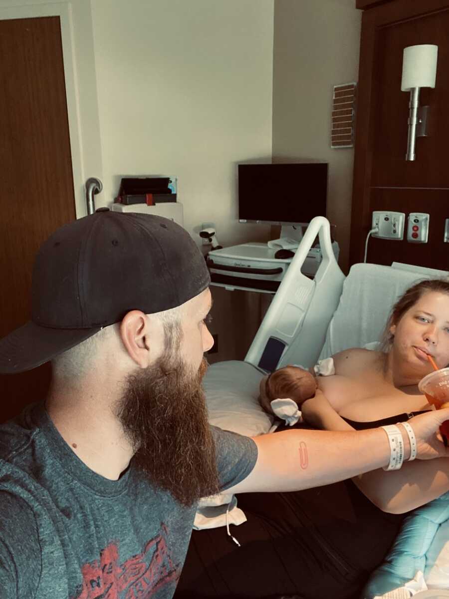 Mother in hospital sips drink while holding her baby