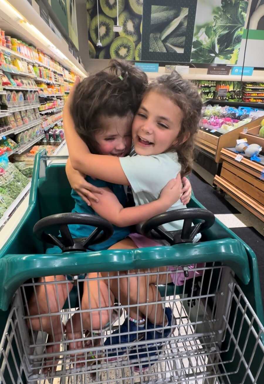 Sisters snuggle while riding in grocery cart together 