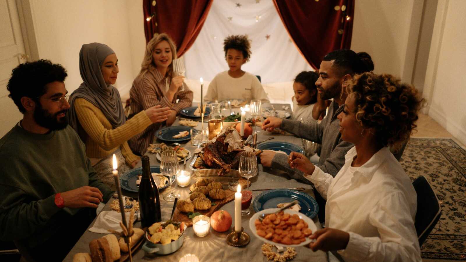 a group of people of different races sit together at a table for a holiday dinner