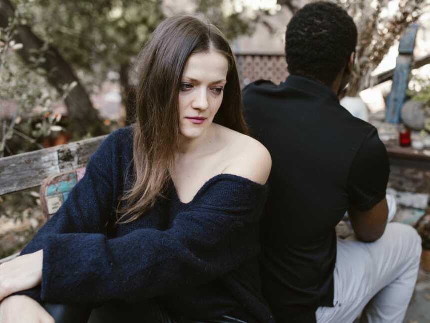 a sad woman sits with her back facing the back of an ex-boyfriend