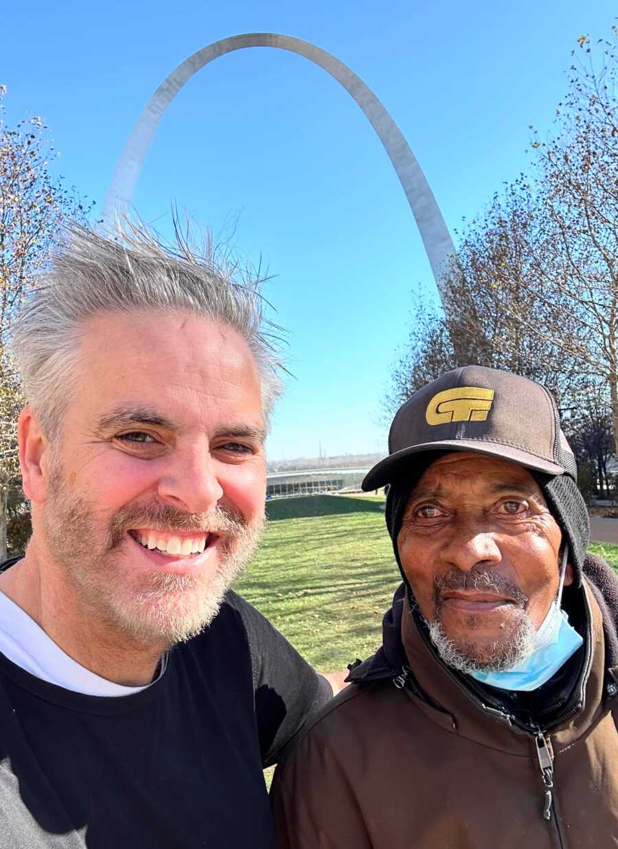 Man smiling next to homeless man in black hat