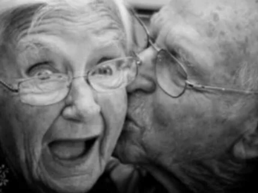 Elderly woman smiling while husband kisses cheek