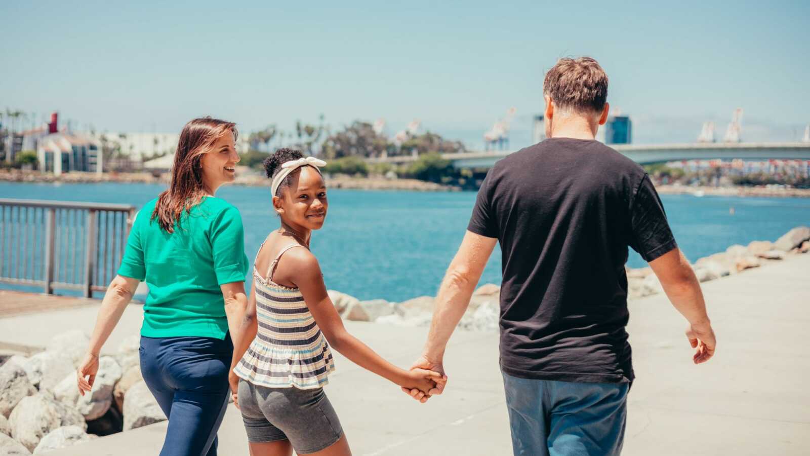 a teen girl walks hand in hand with her adoptive parents on the beach