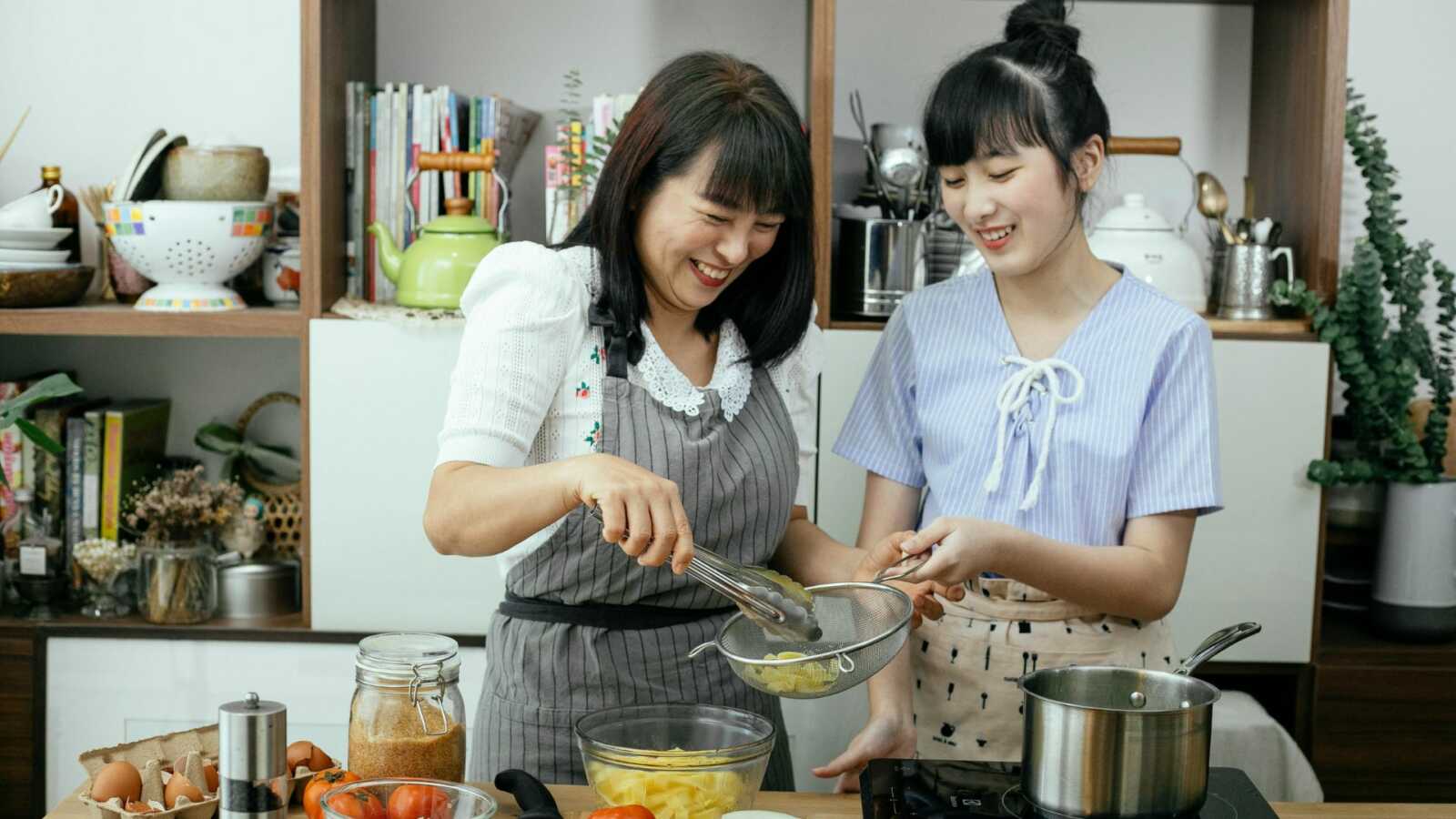 a mother and daughter cook together in a kitchen with vegetables on the counter