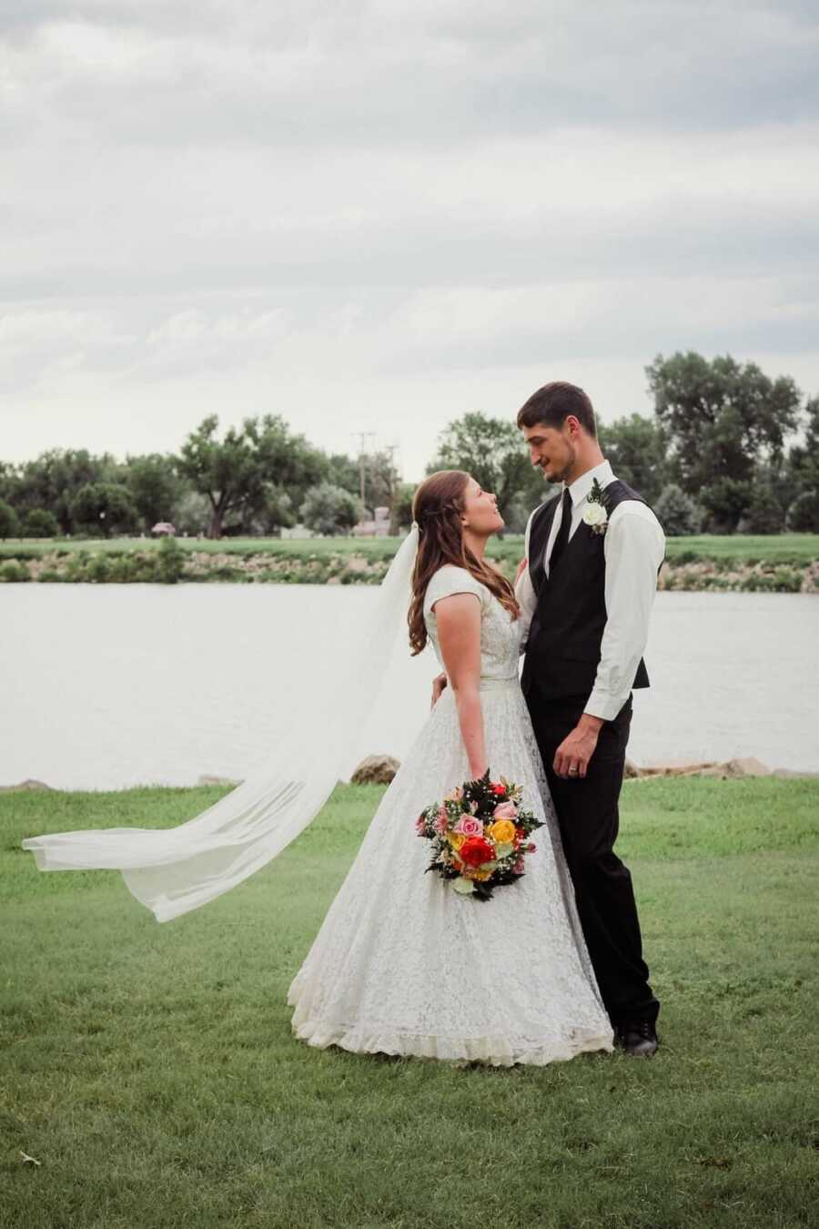 Smiling bride and groom standing beside lake