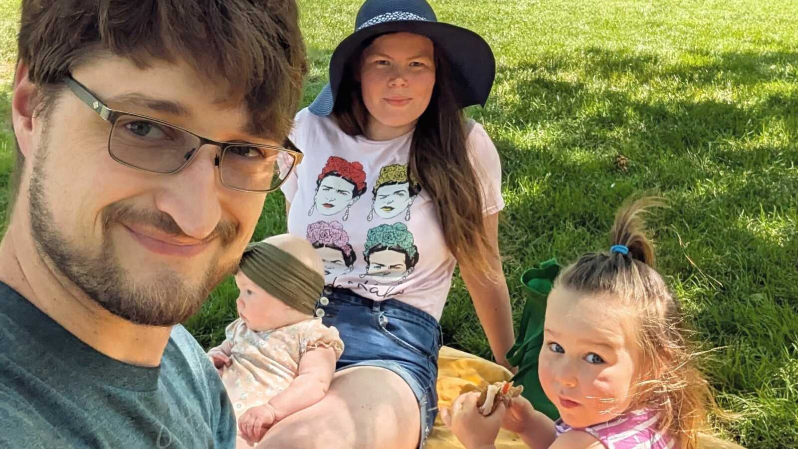 Parents and two kids sitting on yellow picnic blanket in grass