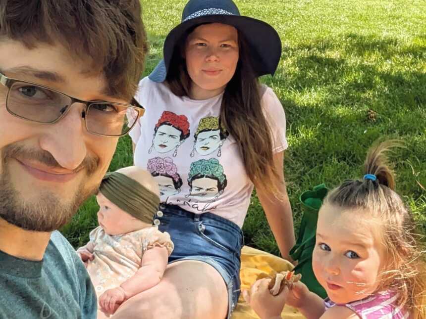 Parents and two kids sitting on yellow picnic blanket in grass