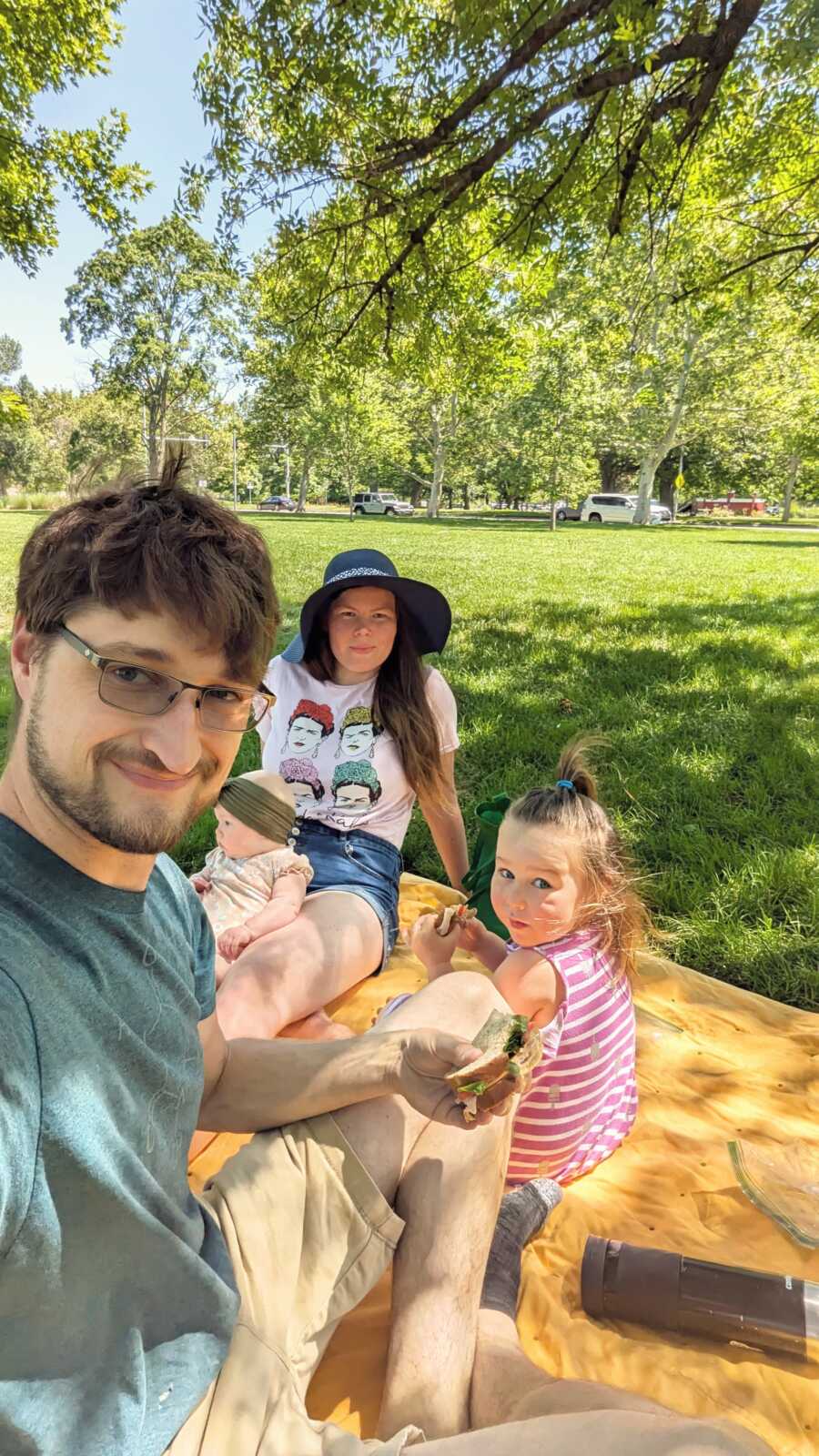 Family sitting on yellow picnic blanket at park