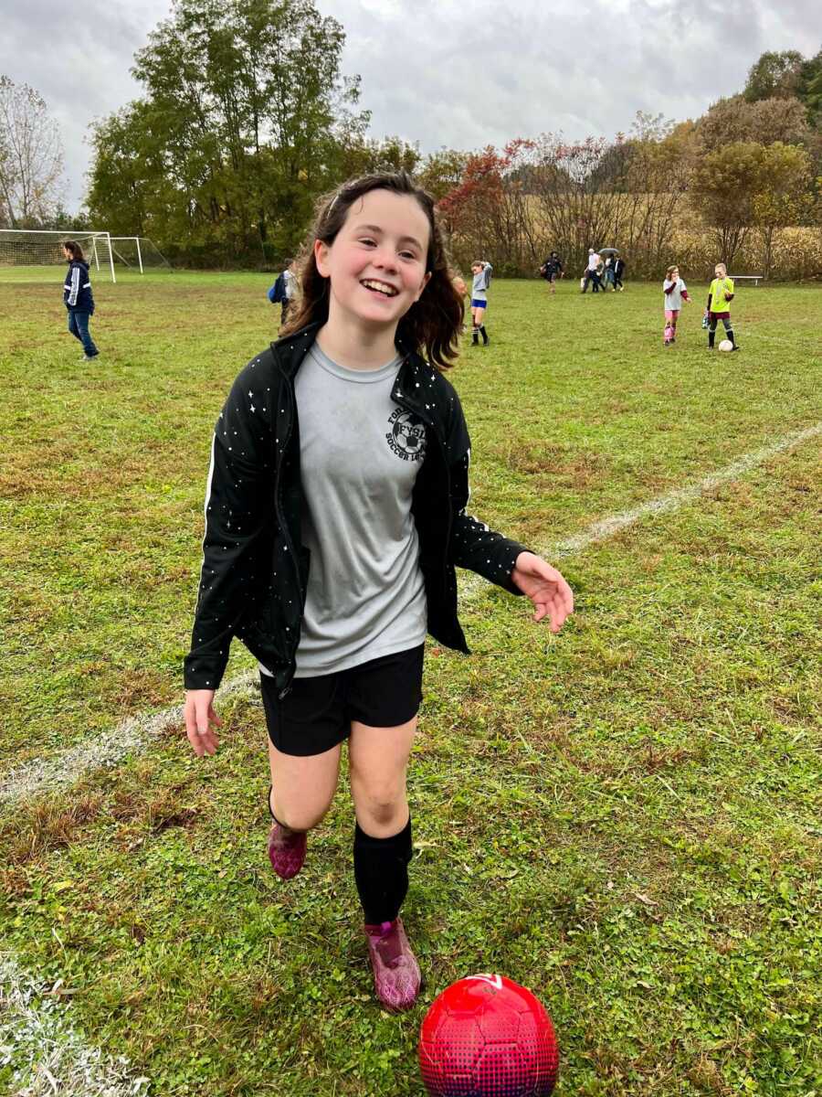 Smiling girl playing soccer on grassy field